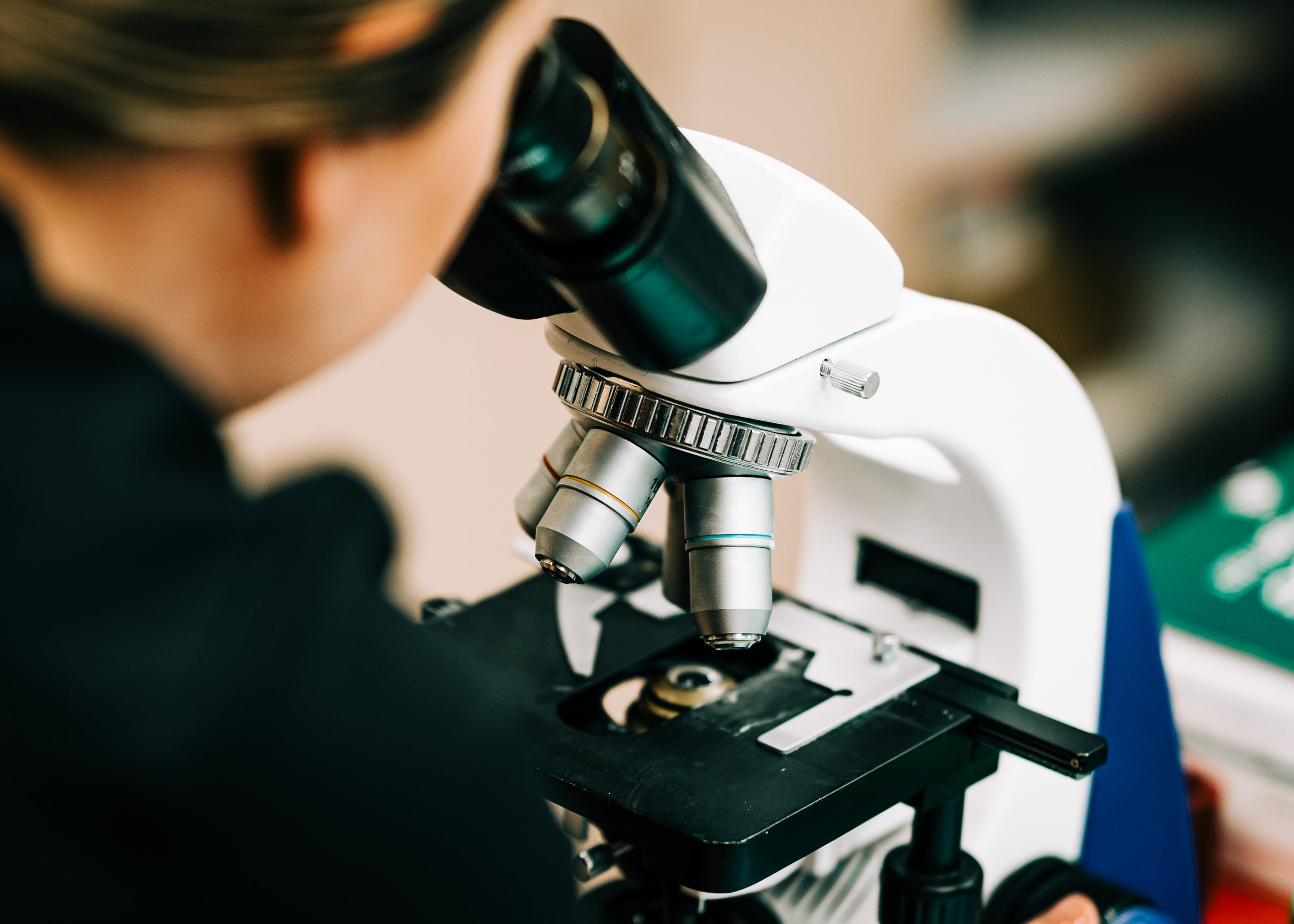 Nurse looking through a laboratory microscope at genetic testing  