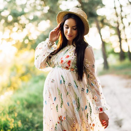 Pregnant woman outside wearing colorful flower dress and fancy top hat